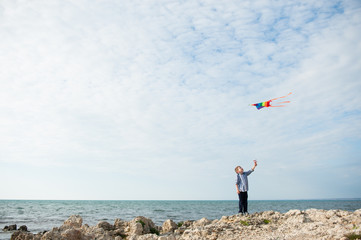one cute small boy holding a kite flying in the sky on the background of ocean - Powered by Adobe
