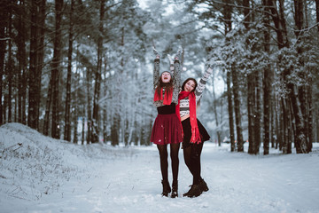 Close up fashion portrait of two sisters hugs and having fun, ride on sled in winter time forest, wearing sweaters and scarfs,best friends couple outdoors, snowy weather