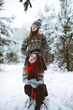  portrait of two sisters hugs and having fun, drinking tea winter time,wearing red santa hats and sweater,best friends couple outdoors, snowy weather