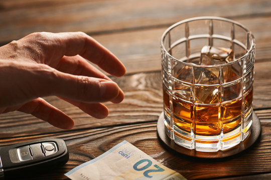 Man's hand reaching to glass with alcohol drink and car key. Drink and drive concept.