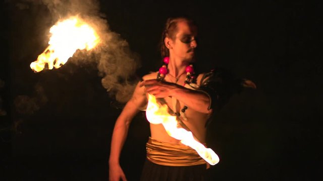 Fire show performance. Handsome male fire juggler performing contact manipulation with fire torch with two lights