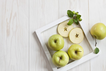 Green apples in  white frame on  white wooden background. Background, top view.