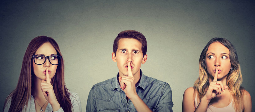 Secretive young people man and two women with finger to lips gesture
