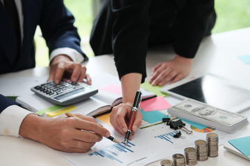 Business man and women are use pen pointing data together and have many coin, dollar cash, tablet, calculator decorate on white table, Closed up, Business and finance concept.