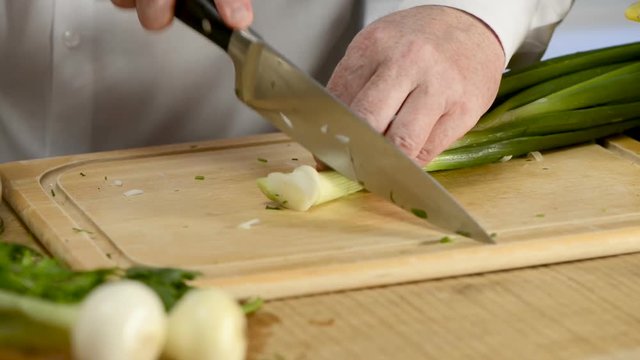Hands of the cook knife big kitchen a fresh green feather onions on a chopping board from a tree