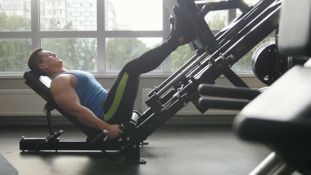 Fitness club - muscular man exercising on leg press machine - side view