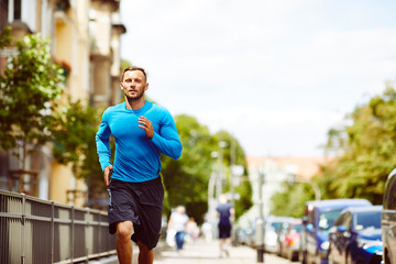 Front view of an athletic man jogging beside a busy city street