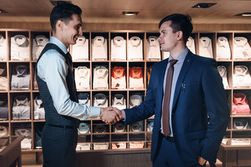 Two business men shake hands with each other in a clothing store against a shelf 