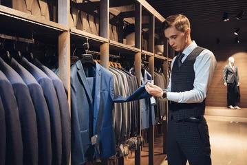 client handsome young businessman in a costume shop inspects the material of the sleeve of the jacket © artpodporin