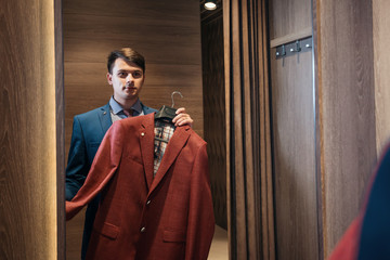 buyer tries  red color of the suit to face, standing in the dressing room at the mirror