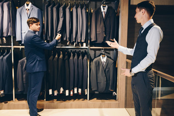 A colleague advises in choosing a suit in a store of luxury clothes for trousers 