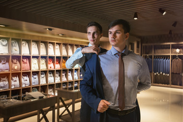 One elegant man helps another try on a suit in a clothing store.