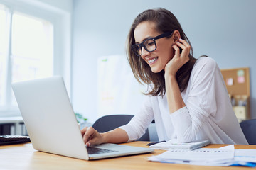 Portrait of veautiful cheerful young businesswoman working on laptop and laughing in home office - obrazy, fototapety, plakaty