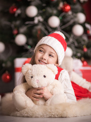 Lovely girl sitting on the floor near the Christmas tree with a bear, studio shot, toning in vintage style.