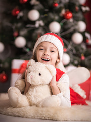 Lovely girl sitting on the floor near the Christmas tree with a bear, studio shot, toning in vintage style.