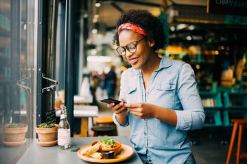 Smiling woman taking photos of her food in a cafe - Powered by Adobe