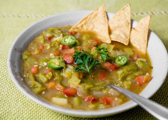 Mexican chili pepper stew on tan bowl decorated with yellow corn tortillas on green tablecloth served with spoon – ethnic food concept