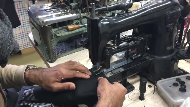 Hands of professional tailor using buttonhole machine on fabric in traditional tailors shop. Real people