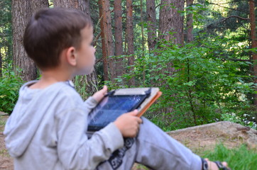 Boy Child playing with Tablet PC Outdoor with forest on background Computer Game Dependence concept