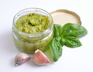 Pesto sauce in a glass jar with basil and garlic.