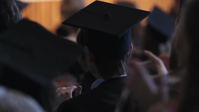 Excited alumnus in mortarboard applauding rector's speech at graduation ceremony