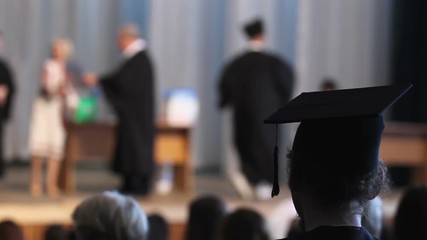 Student looking on stage at graduation ceremony, people receiving diplomas