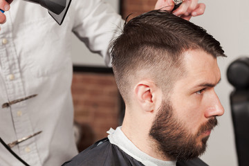 Fototapeta premium The hands of barber making haircut to young man in barbershop