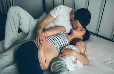 Pregnant woman kissing her partner while their son sleeps