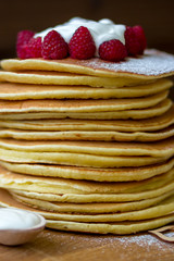 Tasty homemade pancakes with cream and raspberry. On wooden table. Village kitchen