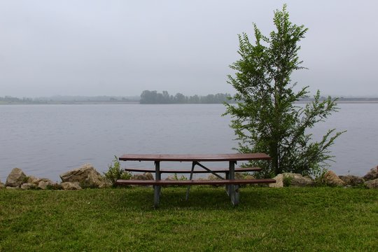Early morning at the lake with a empty picnic table and the fog over the lake.