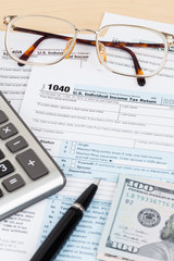 Tax form with calculator, pen, glasses, and dollar banknote