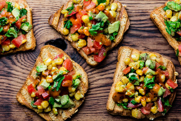 Mexican Latin American style open sandwiches. Vegetarian toasts with maize, avocado, tomatoes on wooden board. Rustic wooden blue background. Top view