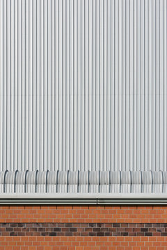Backsteinmauer mit Metalldach vor einer Lagerhallenwand aus Blech