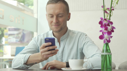 Man using app on smartphone drinking coffee, texting on mobile phone