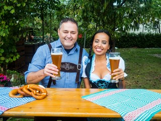 Oktoberfest - multicultural couple in traditional bavarian clothes is sitting in the garden