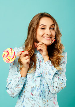 Young pretty smiley woman holding lollipop in hands over blue background