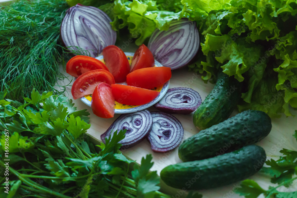 Wall mural Beautiful green greens with cucumbers and chopped red tomatoes and onions.