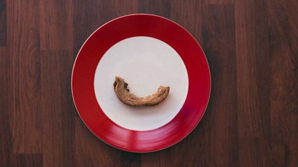 a white and red plate on a wooden background with a eaten bread crust in the middle of the plate