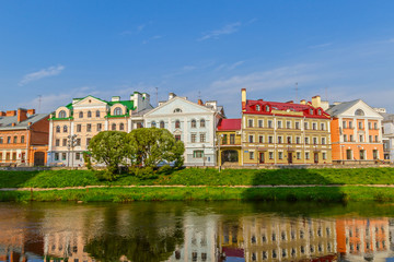 Fototapeta na wymiar View of the old street by the river in the center of the city with reflection in the water. Pskov, Russia