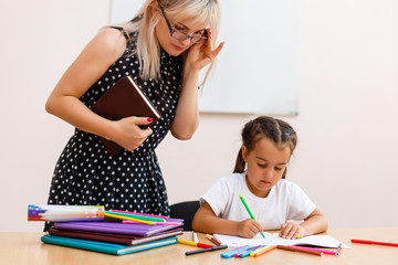 The little girl is studying. School kids work at lesson. Teacher controlling learning process.