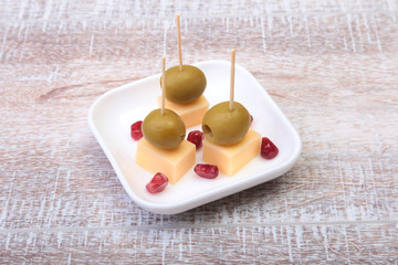 Cheese canapes with olives and Grains of pomegranate on wooden tray close up.
