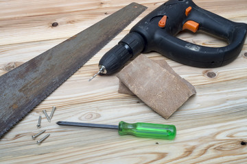 Screwdriver and a screw with the saw and the power drill on wooden table.