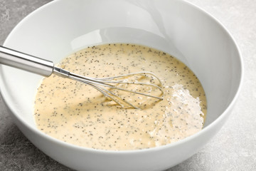 Raw dough with poppy seeds and whisk in bowl on kitchen table