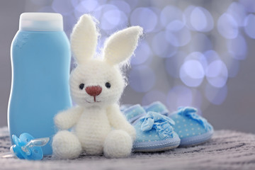 Knitted toy bunny, baby shoes and cosmetics on blurred background