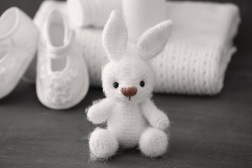 Cute knitted toy bunny and baby accessories on gray background