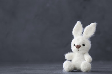 Cute knitted toy bunny on gray background