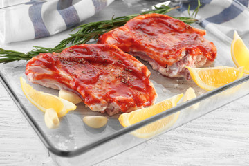Pork ribs with tomato sauce and lemon slices in glass baking tray on table