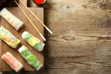 Board with delicious spring rolls on wooden background