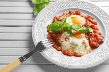 Plate with eggs in purgatory on wooden background
