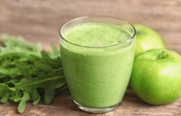 Glass of green smoothie, arugula and apples on wooden table